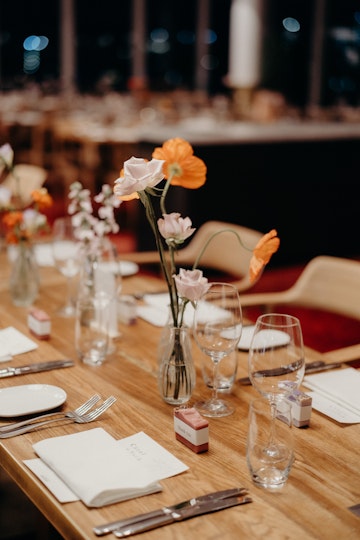 Tables decorated by small vases of flowers and small individual boxes at each setting along with glasses, cutlery and crockery.