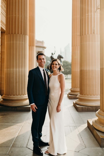 A couple stand between large sandstone columns.