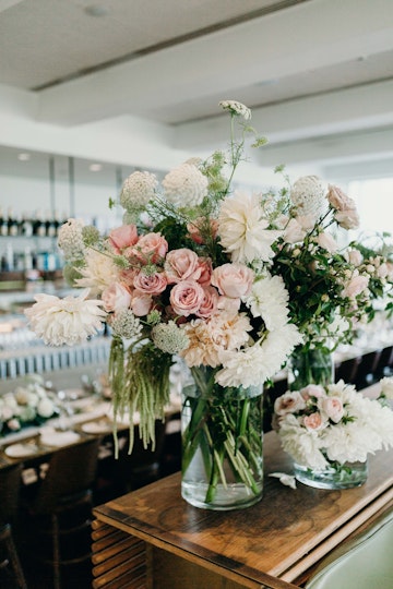 Glass vases filled with pale pink and white flowers on a table in a restaurant.