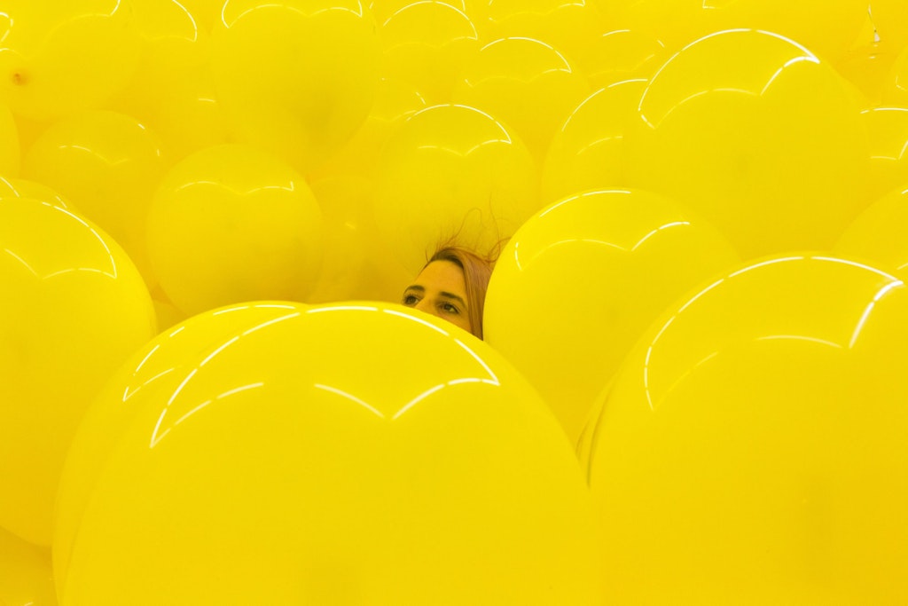 The top of a person's head is visible between a mass of large yellow balloons.