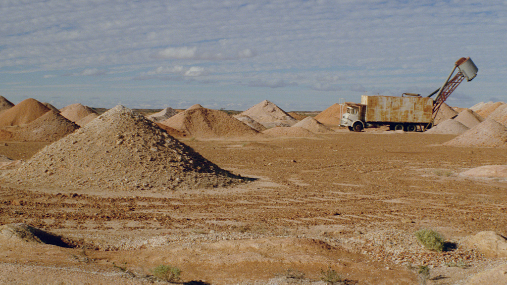A truck among triangular mounds in a barren, sandy landscape.