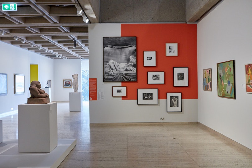 A gallery space with multiple works of art hanging on the walls and sculptures on plinths.