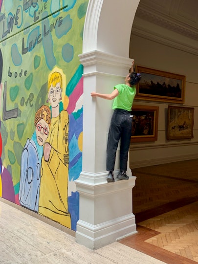 A person stands on a small ledge in a large archway between two rooms in a gallery.