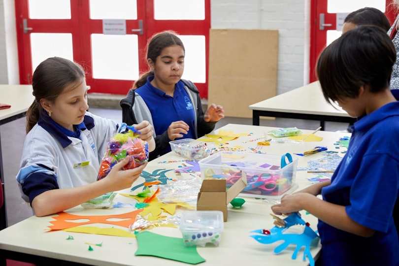 A group of students at a table decorate masks using various materials.
