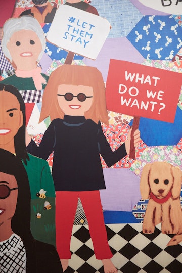 A figure with fringed hair and glasses holds up a sign that says 'What do we want?'. Next to them on one side is a dog, on the other are other figures, one of whom holds a sign that says '#Let them stay'.
