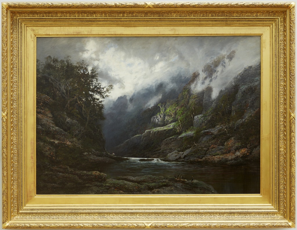 A gold-framed painting of a river running through a steep valley under a brooding sky.