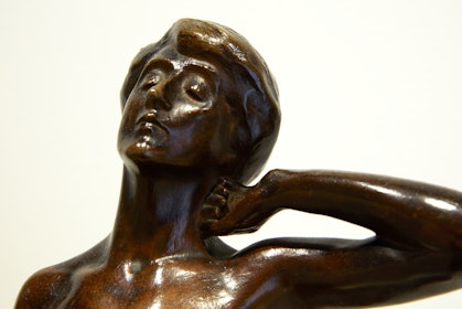 The head and shoulders of a bronze figure. Their eyes are closed, their head leans back and their left hand rests on the side of their neck.