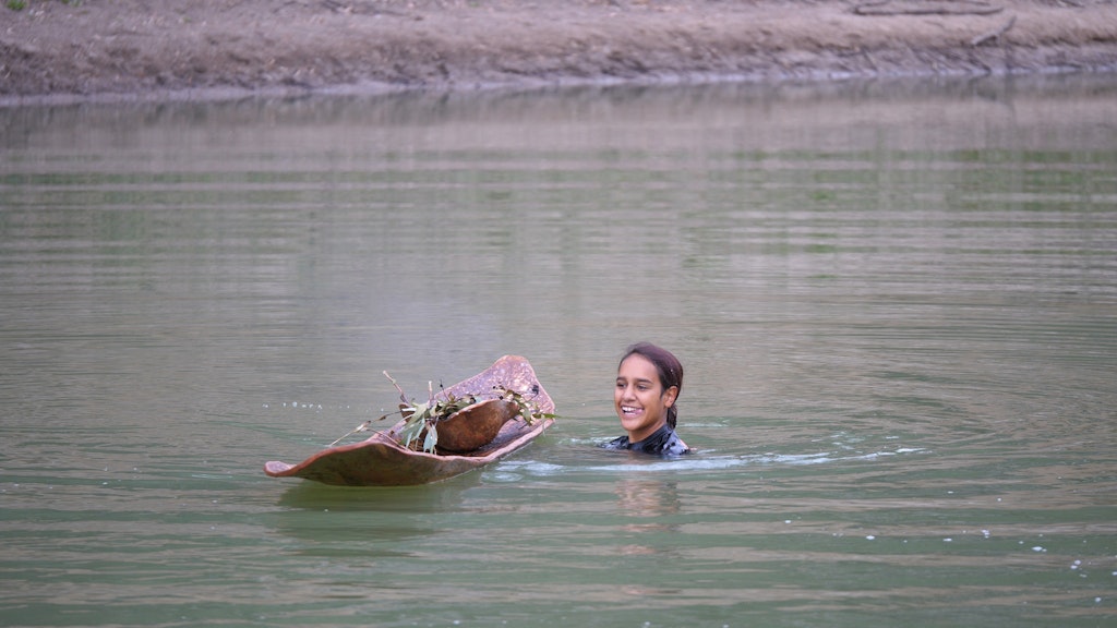 The head and shoulders of a person in water next to a floating bark canoe.