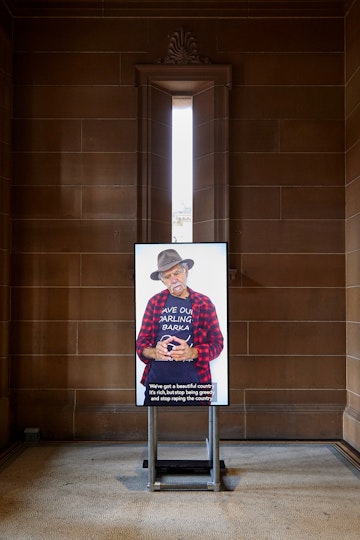 An easel holds an image of a person wearing a hat and checked shirt. There is text across the bottom of the image.
