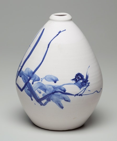 A white egg-shaped ceramic vase with a small bird on a branch painted on it in blue.