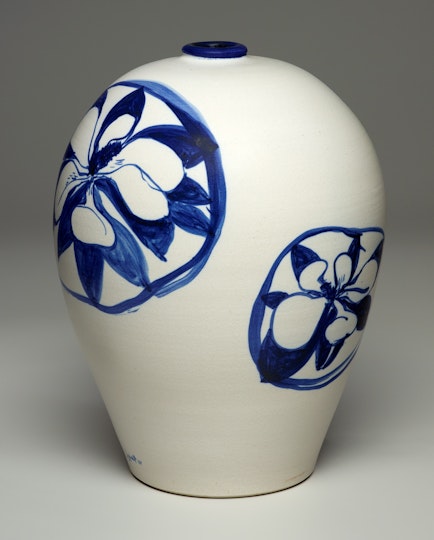 A white ceramic vase with flowers within circles painted on it in blue.