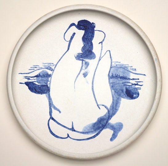 A white ceramic circular plate with a seated nude figure painted in blue.
