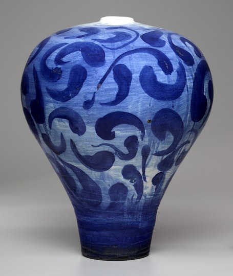 A curved ceramic vase with painted blue arabesque patterns.
