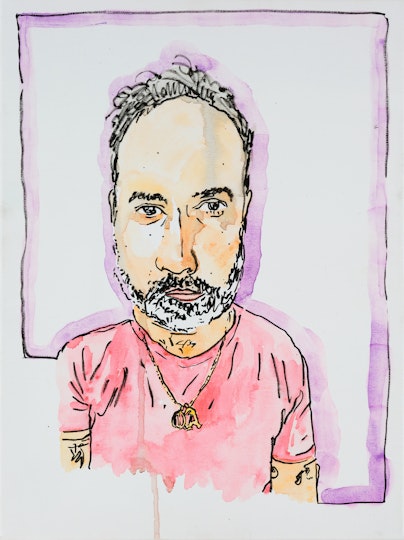 A bearded person with short hair wearing a pink t-shirt and a necklace