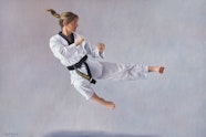 A ponytailed person wearing a martial arts uniform in a side-kick jump
