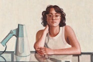A person with shoulder-length hair and glasses sits at a glass table on which rests a loud hailer.