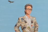 A person with glasses, wearing a newsprint suit, stands with their hands on their hips. A bird flies above.