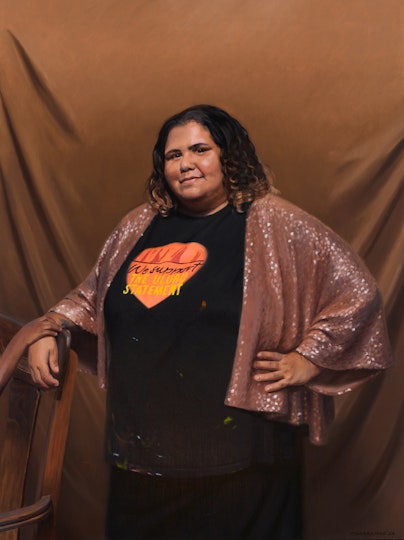 A person with curly shoulder-length hair wearing a t-shirt saying 'We support the Uluru Statement'