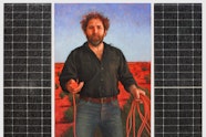 A bearded person wearing black stands in the desert holding a red power chord. On each side are solar panels.
