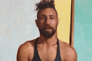 A bearded person with a top-knot of hair, wearing a sleeveless top.