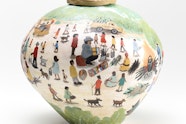 A round ceramic vessel painted with scenes of people at a picnic with three sculptured figures on top of the lid.