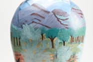 A ceramic vessel painted with a landscape and topped with two sculpted birds.