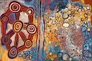 An Aboriginal painting depicting sites and stories using circles and lines, mainly in bold shades of orange, yellow and blue.