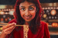 A long-haired person wearing a t-shirt sits at a table under lanterns, using chopsticks in their right hand to hold up noodles from a bowl of food