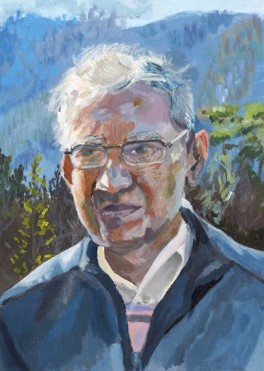 A short-haired person wearing glasses, a collared t-shirt and jacket. In the background are trees and mountains.