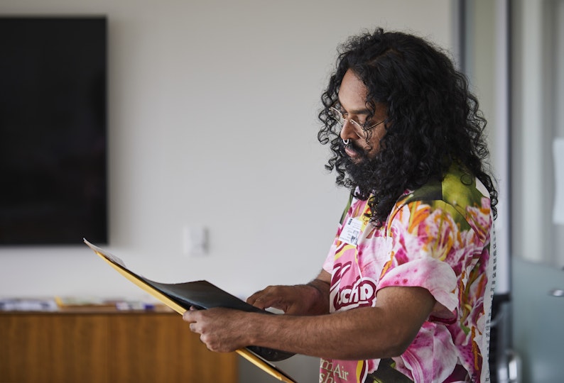 A long-haired person with glasses looks at a piece of paper