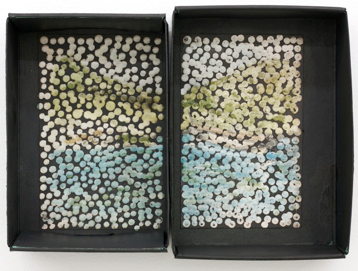 A view into two rectangular boxes, side by side, the bases of which are painted with a white, green and blue dots that form a contiguous image