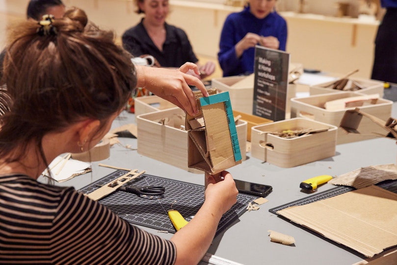 Several people seated at a table making cardboard structures