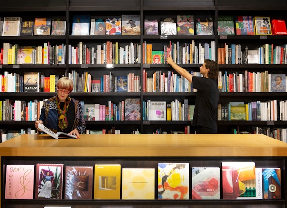Two people browsing bookshelves in the Art Gallery of NSW shop.
