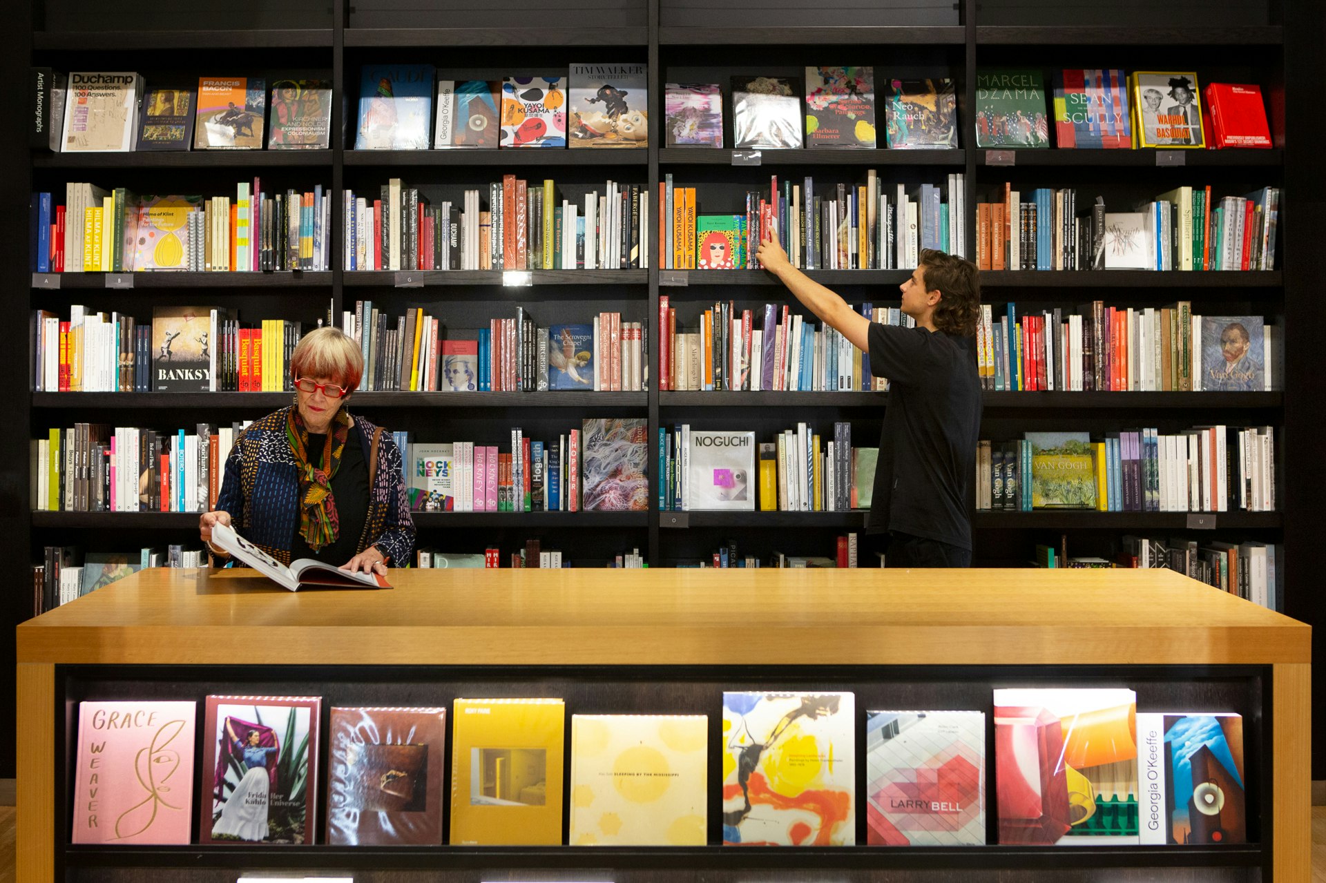 Two people browsing bookshelves in the Art Gallery of NSW shop.