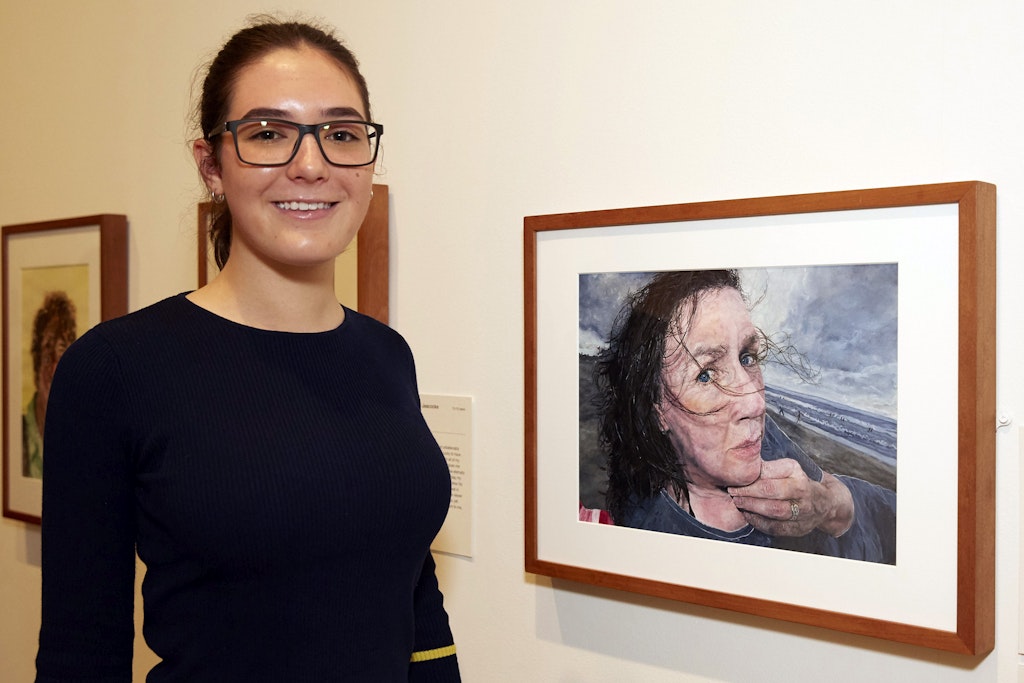 A person in glasses stands next to a framed portrait of a person lying down at the beach
