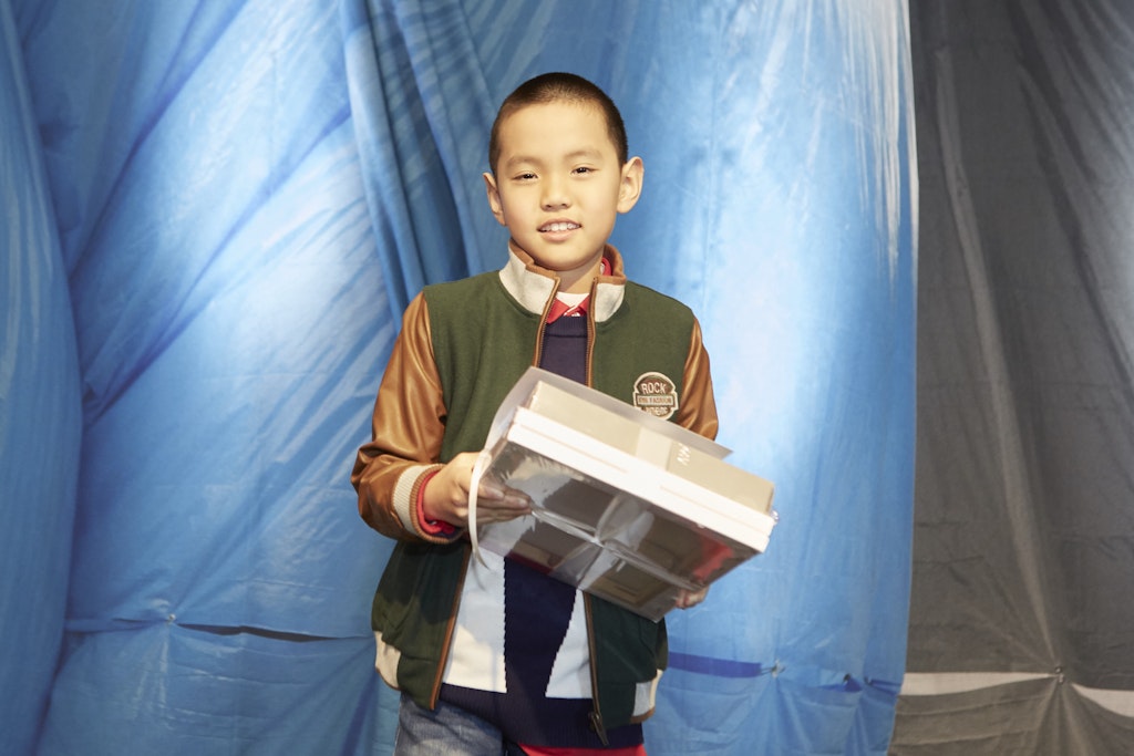 A young short-haired person stands holding a bundle