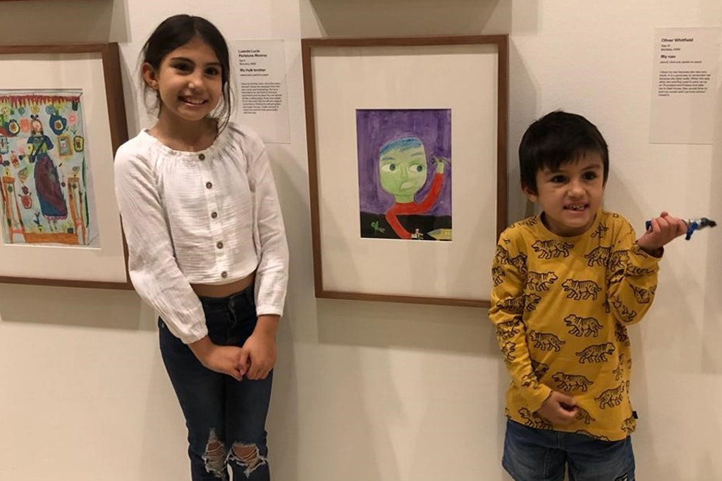 Two children stand either side of a framed portrait of a green-skinned person
