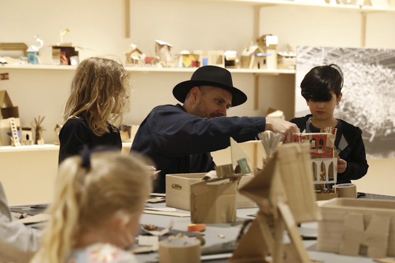 An adult and three children at a table making cardboard structures
