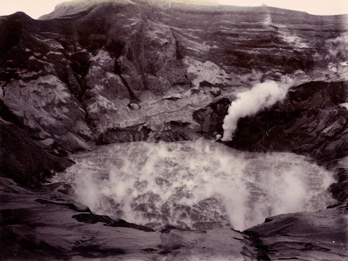Black-and-white photograph looking into a steaming volcanic crater