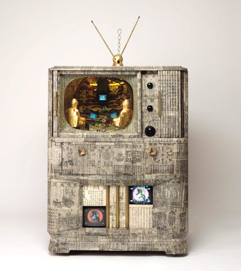 Two gold buddhas sit inside the screen section of a TV unit covered with newspaper