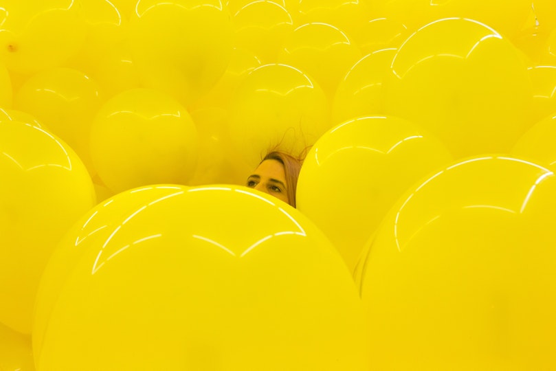 A person's head among a dense cluster of yellow balloons