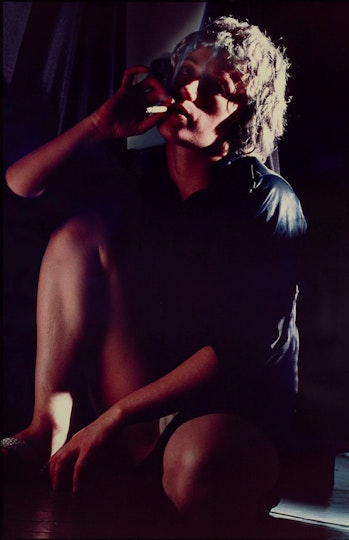A person wearing dark clothing with bare legs sits smoking a cigarette