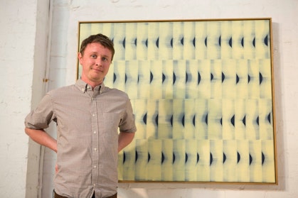 A person stands in front of  a large abstract painting of repeated pattersn