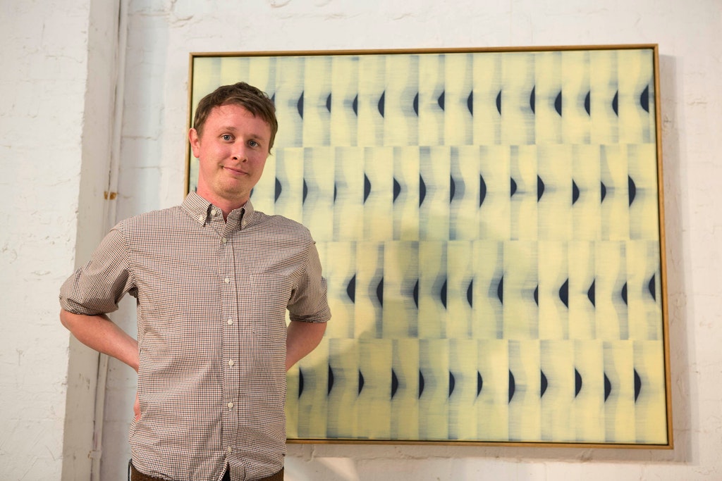 A person stands in front of  a large abstract painting of repeated pattersn