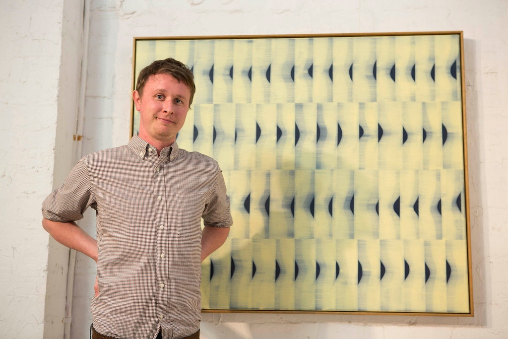 A person stands in front of a large abstract painting of repeated pattersn