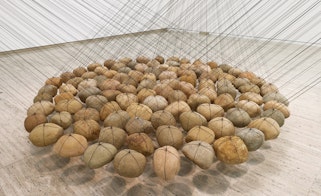 Dozens of rounded stones of similar size suspended by strings in a tight grouping above the floor