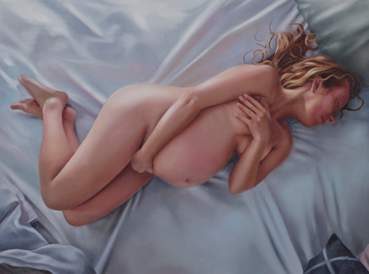 A nude pregnant person lies on a bed