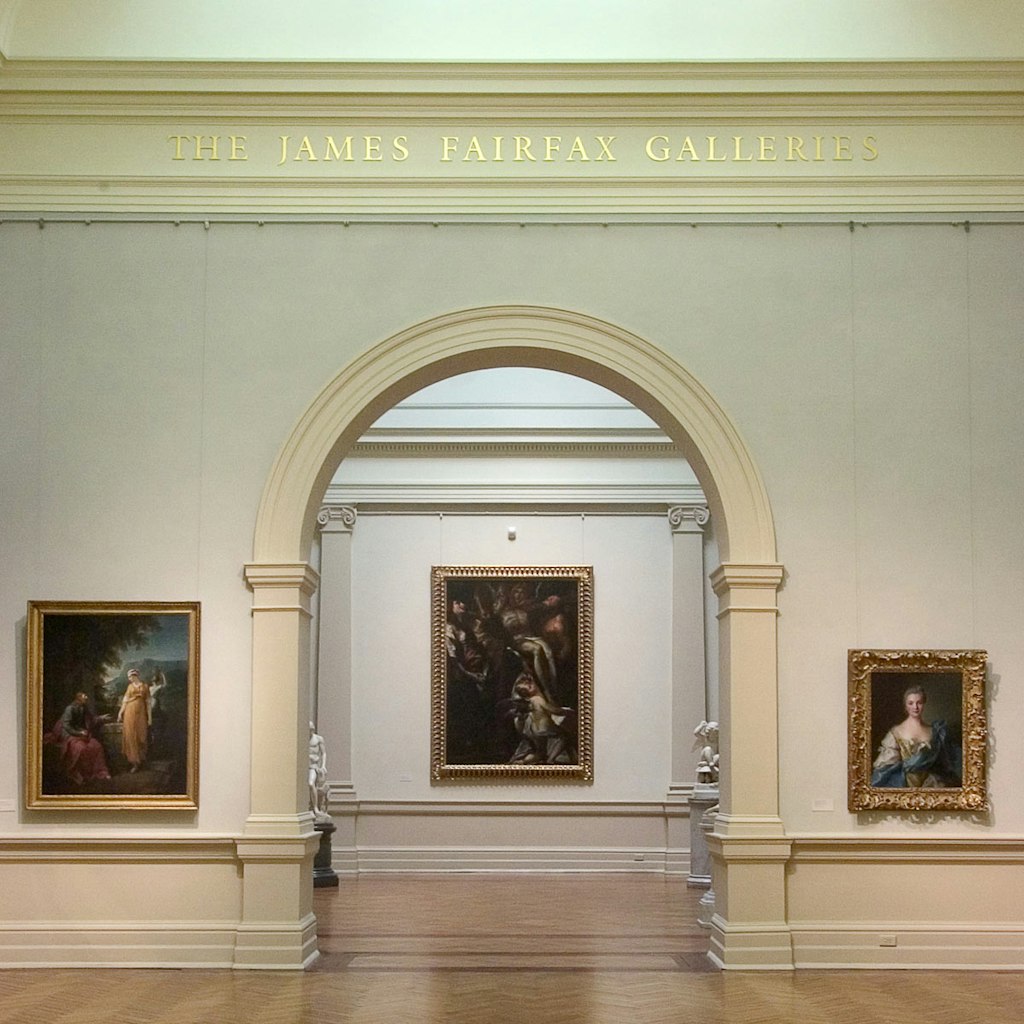 Three paintings hang on the wall of a gallery with a central archway, above which a sign reads 'The James Fairfax Galleries'