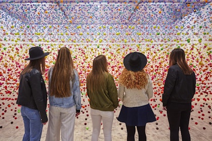 Five people look at a room full of small coloured balls suspended in the air