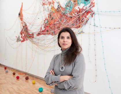 A person stands in front of a wall with an inverted map of the world made from coloured thread, with balls of thread are attached